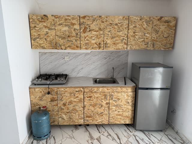 Cuisine équipée : plaque de cuisson à gaz, évier, plan de travail et crédence en marbre, réfrigérateur et rangements en bois clair.